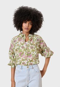 Camicia button-up a motivi floreali con disegni rosa e verdi, maniche corte e una vestibilità rilassata. Indossata con pantaloni corti in denim chiaro a vita alta.