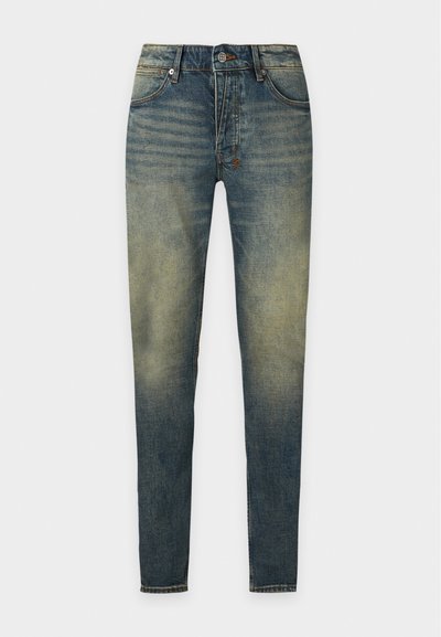 Jean slim bleu avec des zones décolorées aux cuisses et aux genoux, poches avant, fermeture par boutons et passants de ceinture sur fond uni.