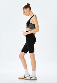 Sostén deportivo negro con detalles en gris, pantalones cortos negros de tiro alto y zapatillas blancas con rayas negras. Material suave y ajustado, sin patrones.
