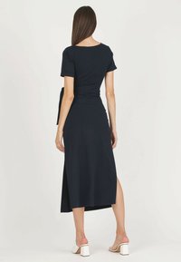 Marina maxiklänning med korta ärmar, sidoflik, och knytning i midjan. Slät tygtextur, avslappnad passform och lätt stretch.