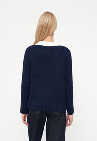 Pulover bleu marin, țesătură texturată, croi lejer, tiv ribbelat, decolteu larg, detaliu cu guler alb, mâneci lungi. Purtați cu blugi închiși la culoare.