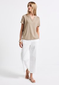 Beige top s krátkým rukávem a výstřihem do V, kombinovaný s bílými kalhotami s širokými nohavicemi a tanovými sandály na pásky. Hladký materiál a uvolněný střih.