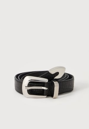 Ceinture noire en cuir synthétique effet croco avec boucle et embout métalliques argentés brillants, enroulée sur un fond clair uni.