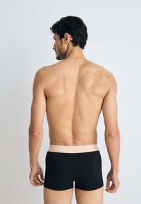 Boxer shorts noirs avec une ceinture en logo Lacoste rose clair, design ajusté et texture lisse, présentés de dos sur un fond neutre.