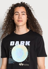 Čierne bavlnené tričko s veľkým grafickým potlačou a textom "TMAVÁ STRANA MESA" spolu s farebným dizajnom mesiaca. Krátke rukávy s logom.