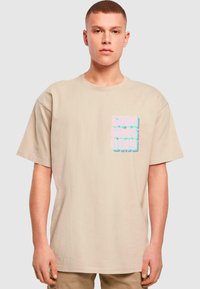Béžové bavlněné tričko s krátkým rukávem. Na přední straně se nachází text "Good Vibes Only" v pastelových barvách, napsaný tučným, výrazným písmem.