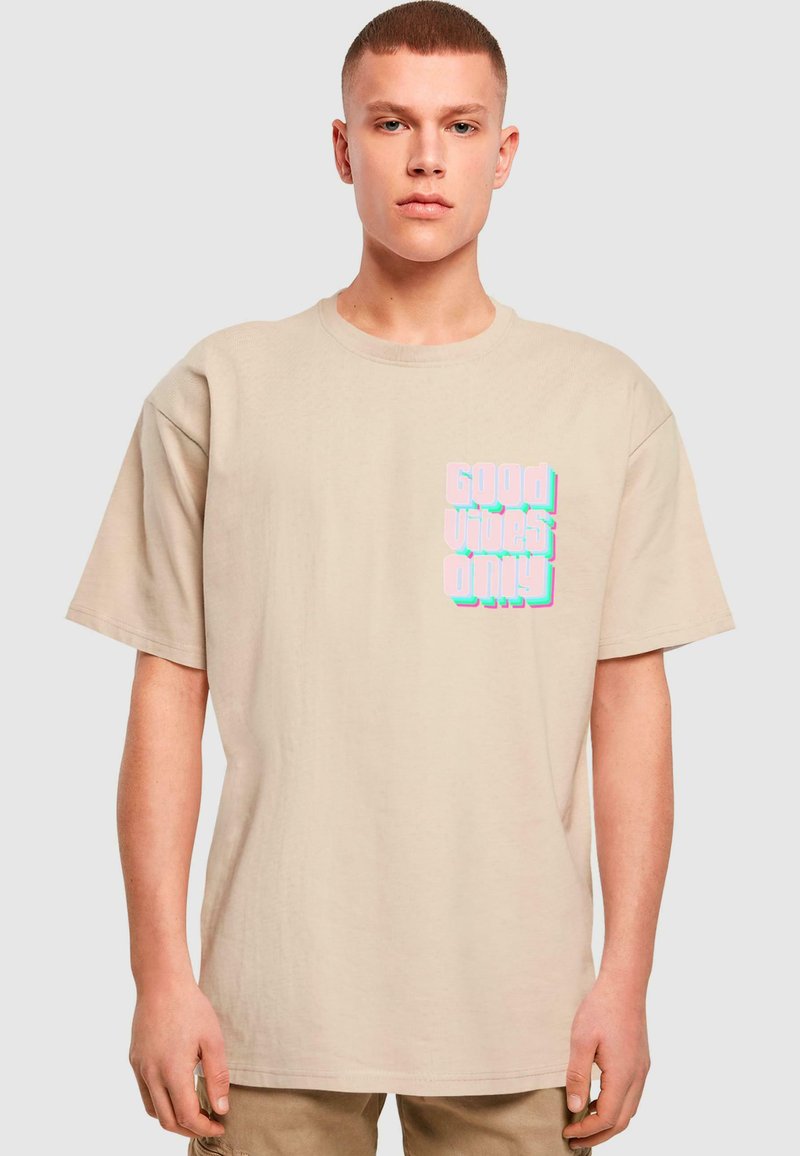 Béžové bavlněné tričko s krátkým rukávem. Na přední straně se nachází text "Good Vibes Only" v pastelových barvách, napsaný tučným, výrazným písmem.