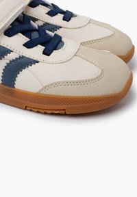 Scarpe sportive beige con accenti blu navy, in pelle texturizzata e suola in gomma. Presentano dettagli cuciti e un design con lacci.