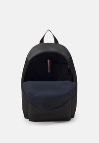 Zaino in tessuto nero con un'apertura rotonda, un interno blu navy e una maniglia superiore. Presenta bordi cuciti e una piccola tasca interna.
