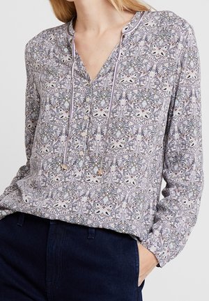 Blouse à manches longues en violet clair avec des motifs floraux et géométriques complexes. Possède un col en V, des détails à cordon et une texture de tissu douce.