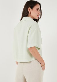Camicia corta a maniche corte verde chiaro, realizzata in un tessuto misto lino testurizzato, con colletto classico e maniche arrotolate, caratterizzata da una vestibilità larga.