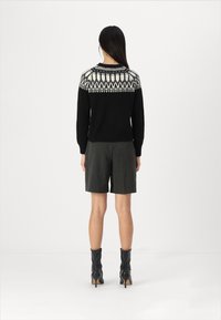 Schwarzer Pullover mit weißem geometrischem Strickmuster an der Passe, kombiniert mit grauen Shorts und schwarzen Ankle Boots mit hohen Absätzen.