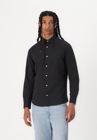 Svart langermet skjorte med krage, med hvite knapper og en skreddersydd passform, kombinert med lyseblå denimjeans.