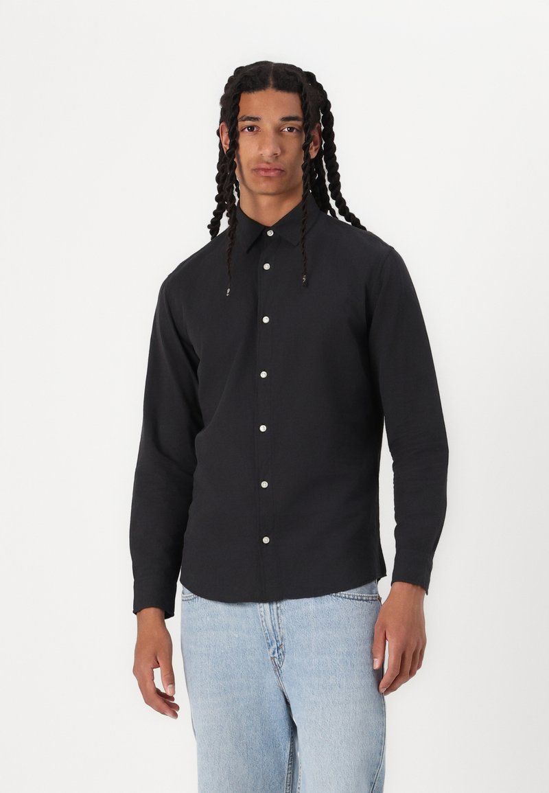 Svart langermet skjorte med krage, med hvite knapper og en skreddersydd passform, kombinert med lyseblå denimjeans.