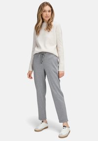 Jasno beżowy sweter dzianinowy z teksturowanym wzorem w diamenty, zestawiony z szarymi spodniami w paski i białymi trampkami na gumowej podeszwie. Swobodny strój.