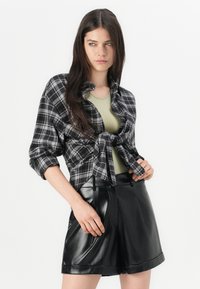 Svart og grå rutete kort skjorte med knytt foran, parret med høyhårede sorte faux skinnshorts. Lys grønn tanktop under.