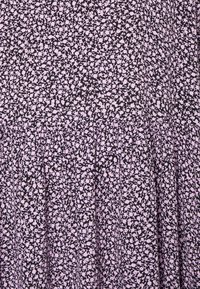 Lila Stoff mit einem floralen Muster und pinken Akzenten. Geraffte Falten sorgen für Textur, während die Oberfläche glatt und das Design leicht ist.