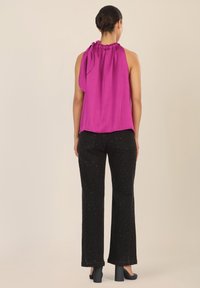 Top morado sin mangas con escote fruncido y detalle de lazo, combinado con pantalones de pierna ancha negros con tachuelas plateadas dispersas y tacones gruesos.