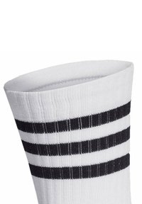 Calcetín blanco de algodón con textura de canalé, que presenta tres franjas horizontales negras en la parte superior. Tela suave, de longitud media hasta la pantorrilla.