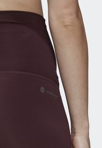Vínové legíny s vysokým pasem vyrobené z hladkého, elastického materiálu. Obsahují AEROREADY branding v kruhovém designu na pasu.