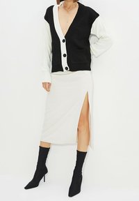 Czarno-biały sweter na guziki z dekoltem w serek i kieszeniami, zestawiony z kremową spódnicą midi z bocznym rozporkiem oraz czarnymi botkami za kostkę.