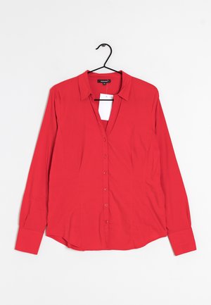 Blusa rossa a maniche lunghe con bottoni e colletto, appesa a una gruccia nera su sfondo bianco, con etichetta del prezzo bianca.
