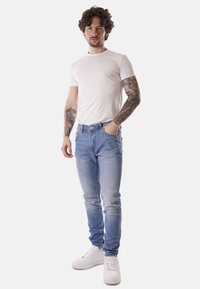 Jeans in denim azzurro chiaro con una vestibilità slim e leggere sfumature, abbinati a una t-shirt bianca aderente e sneakers bianche. Presentano cuciture scure.