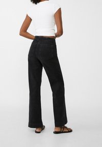 Jeans negros de pierna ancha con piernas rectas prominentes, cintura alta y dos bolsillos traseros. Tela de denim suave con detalles mínimos de costura.