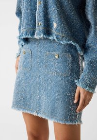 Completo in denim composto da una giacca corta blu con effetto strutturato e bordi sfrangiati e una mini gonna a vita alta abbinata con dettagli in bottoni dorati.