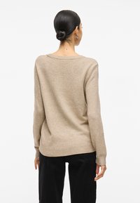 Beżowy sweter dziany o luźnym kroju, szerokim dekolcie oraz żeberkowych mankietach i dolnej krawędzi. Tył swetra ma gładką fakturę i lekko luźny fason.