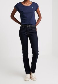 Camiseta de manga corta azul marino con un pequeño gráfico de una palmera verde, combinada con jeans de denim oscuro y zapatillas blancas.