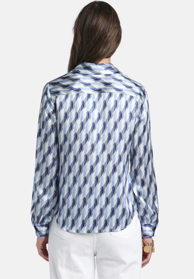Camicia in seta con motivo geometrico nelle tonalità del blu. Senza pieghe, maniche lunghe e colletto classico con orlo arrotondato.
