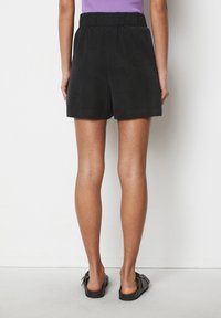 Bermudas negras con cintura elástica, fabricadas con una tela suave. Presentan un diseño simple, hasta la rodilla, sin patrones visibles ni herrajes.