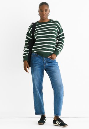 Green and white striped knit sweater, relaxed fit, high-waisted blue jeans, and black sneakers with white stripes, worn with a black shoulder bag.