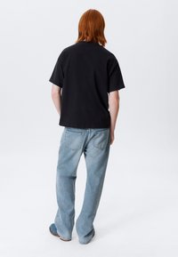 Zwarte katoenen t-shirt met een ontspannen pasvorm, gecombineerd met lichtblauwe wijde jeans. Achteraanzicht toont korte mouwen en eenvoudige ontwerpelementen.