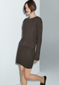 Set in maglia marrone composto da un maglione e una gonna, con un design a trecce testurizzato, maniche lunghe e orlo a coste. Tessuto liscio con una silhouette aderente.