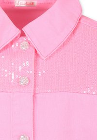 Blouse rose avec un col, une partie supérieure texturée en sequins et un tissu lisse en dessous, ornée de boutons ronds et pailletés.