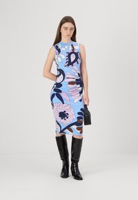 Πλεκτό φόρεμα με μπλε φόντο και λουλουδάτα μοτίβα σε ροζ, σκούρο μπλε και καφέ, συμπληρωμένο με μαύρες μπότες μέχρι το γόνατο και μια μαύρη τσάντα.