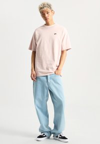 Světle růžové tričko s krátkým rukávem a malým černým logem, v kombinaci s volnými světle modrými džíny a černými teniskami s bílými detaily.