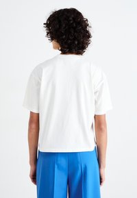 Hvid T-shirt med korteærmer lavet af bomuld, med en afslappet pasform og en rund halsudskæring, parret med blå høj talje bukser.