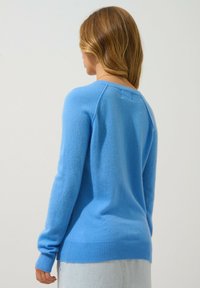 Blå stickad tröja med långa ärmar, ribbade muddar och nederkant. Mjuk textur och en avslappnad passform, med rund halsringning och axelsömmar.