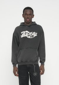 Must kapuutsiga dressipluus, ees tasku, valge graafilise trükiga ja soonikkoes varrukasuutmega. Sobitatud kulunud mustade teksadega, millel on neetidega detailid.