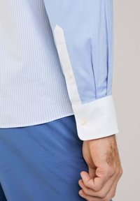 Camisa a rayas azul claro con puños blancos contrastantes, con un cuello clásico y cierre de botones, confeccionada en una tela suave.