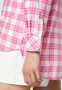 Růžová a bílá kostkovaná košile s dlouhým rukávem a zapínáním na knoflíky, s mírným rozšířením na lemu a hladkým bavlněným materiálem.