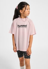 Różowa bawełniana koszulka z okrągłym dekoltem i krótkimi rękawami raglanowymi, z czarnym napisem "hummel PERFORMANCE" na przodzie.