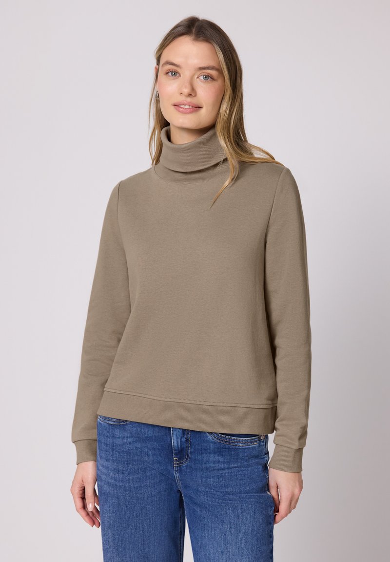 Sweat-shirt à col roulé marron clair en texture côtelée douce, doté de manches longues et d'une coupe décontractée, associé à un jean en denim bleu.