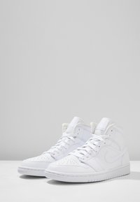 Vita höga sneakers med läderövre del, perforerad tåkappa, platta snörningar, vadderad krage och gummisula med logodetalj på sidan.