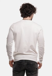 Maglione bianco con maniche lunghe, polsini a coste e orlo dritto, realizzato in materiale morbido. Indossato con jeans scuri.