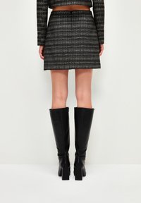 Jupe en tweed noir avec une coupe droite et des accents métalliques, associée à des bottes en cuir noir hautes jusqu'aux genoux avec un talon épais.