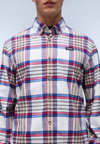 Camisa de cuadros en colores azul, rojo y beige. Presenta un cuello con botones, mangas largas y una pequeña etiqueta con el logotipo en el pecho.